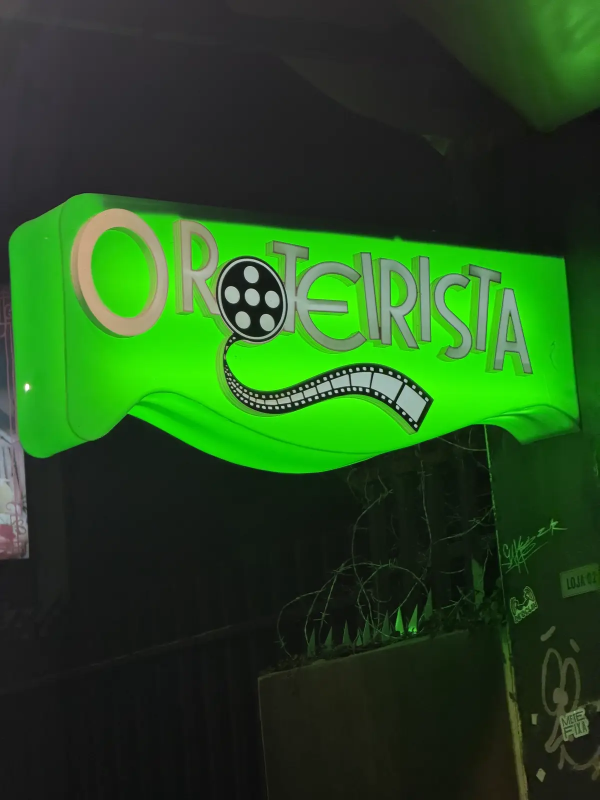 Letreiro neon verde do O Roteirista aceso à noite